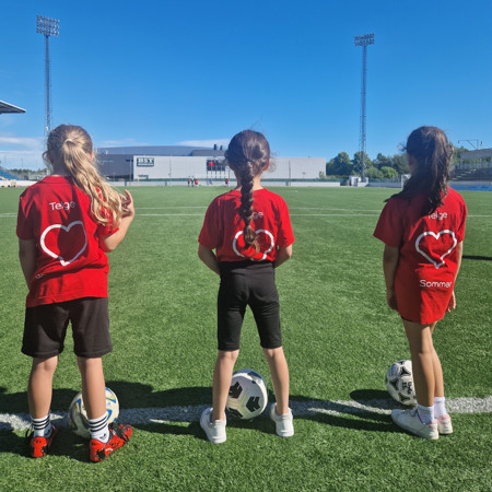 Tre tjejer står på fotbollsplanen med en varsin boll