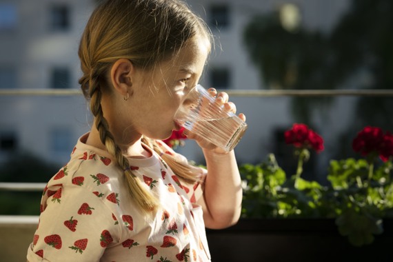 En liten flicka som dricker ett glas vatten.