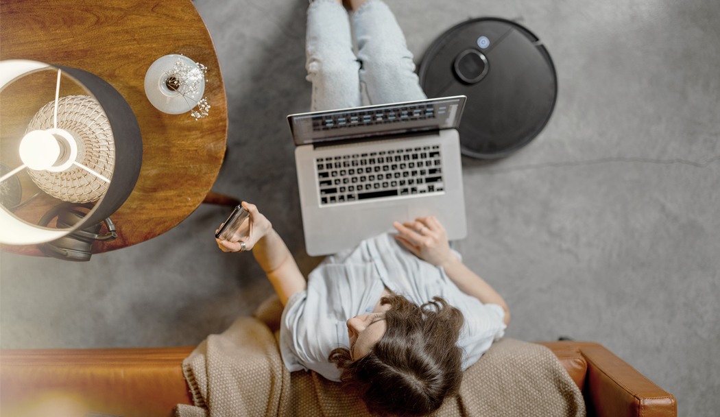 bild tagen ovanifrån på en kvinna som sitter på golvet med en laptop i knät och en mobiltelefon i handen