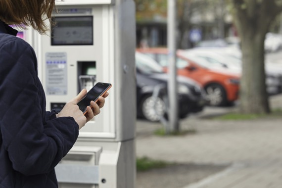 En kvinna som använder en mobiltelefon vid en parkeringsautomat