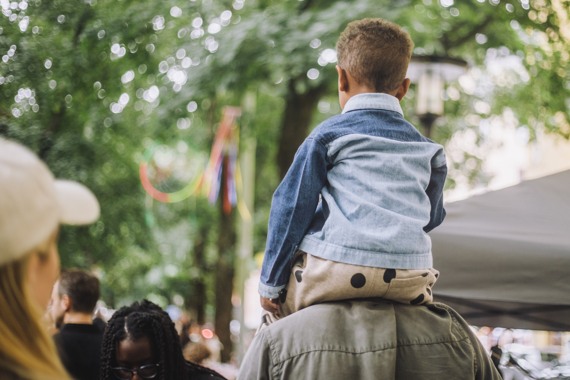 En person med ett barn på axlarna som promenerar i ett festivalområde.