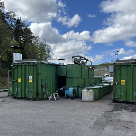 En grupp gröna fraktcontainrar på en parkeringsplats.