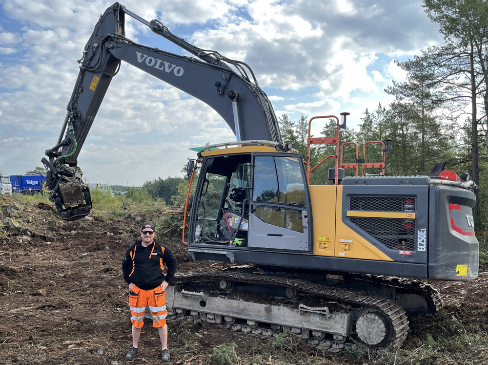 En man står på ett fält bredvid en bulldozer.