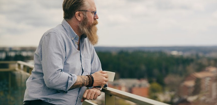 Man som står med en kaffekopp i handen och tittar på utsikten från sin balkong 