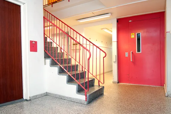 En röd hissdörr och några trappor i en byggnad.