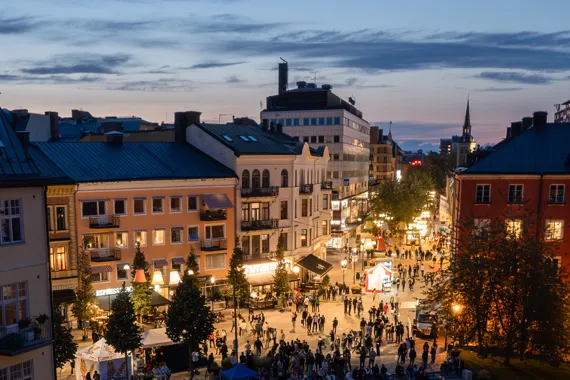 Olof Palmes plats i centrala Södertälje. Gatubelysningen lyser upp gatan och husen. Människor befinner sig på på gatan. 