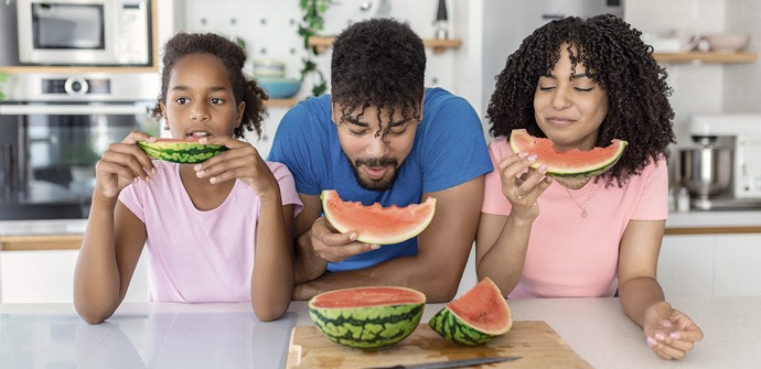 En man och två flickor som äter vattenmelon i ett kök