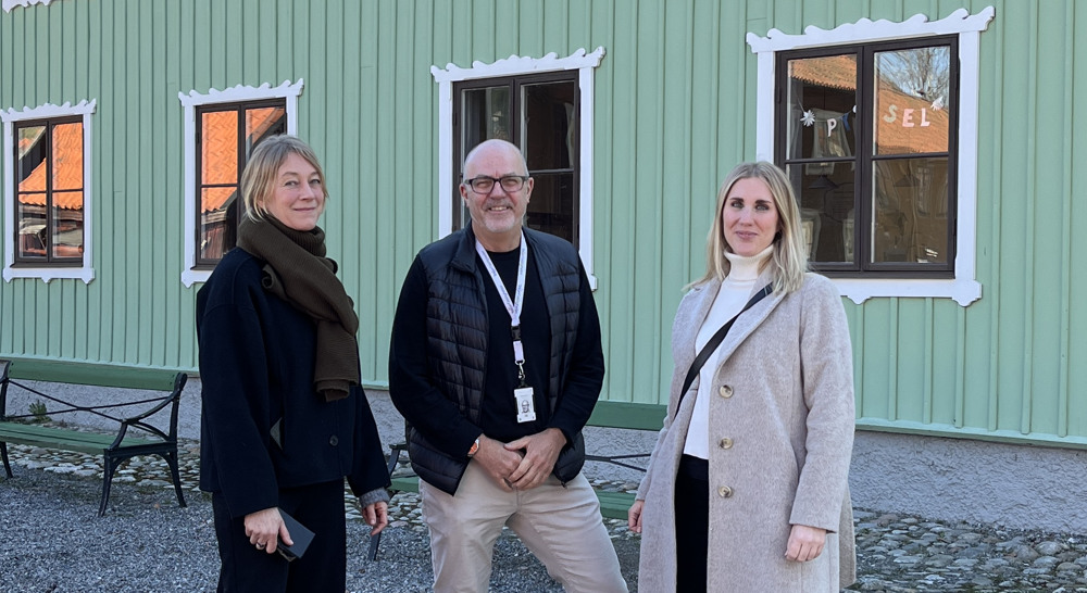 Tre personer står framför en grön byggnad.
