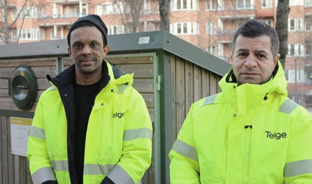Två män i arbetskläder står framför en sopcontainer