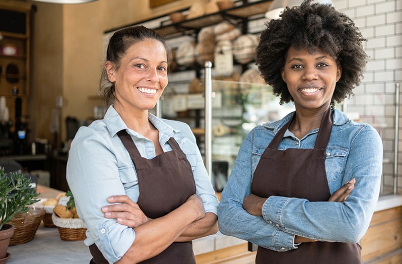 Två kvinnor i bruna förkläden i ett bageri
